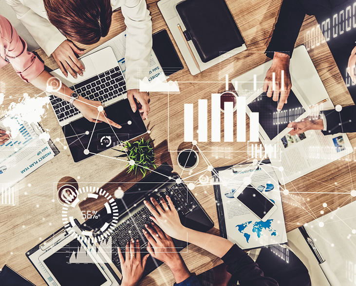Top-down view of a diverse team working together at a table with laptops, tablets, and charts, overlaid with digital data graphics