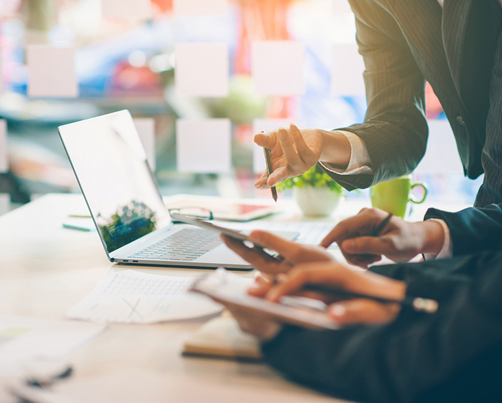 Close-up of business professionals discussing data and strategy at a desk with a laptop, tablet, documents,