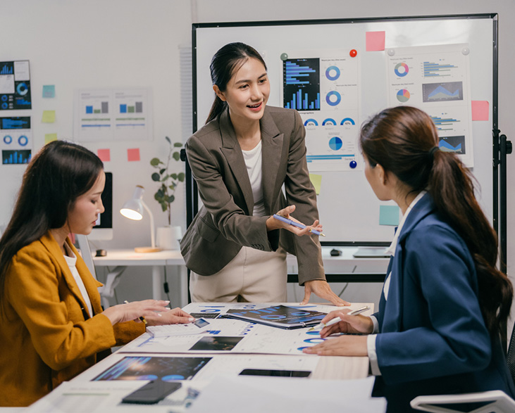 Three businesswomen in a meeting room discussing data charts and digital reports